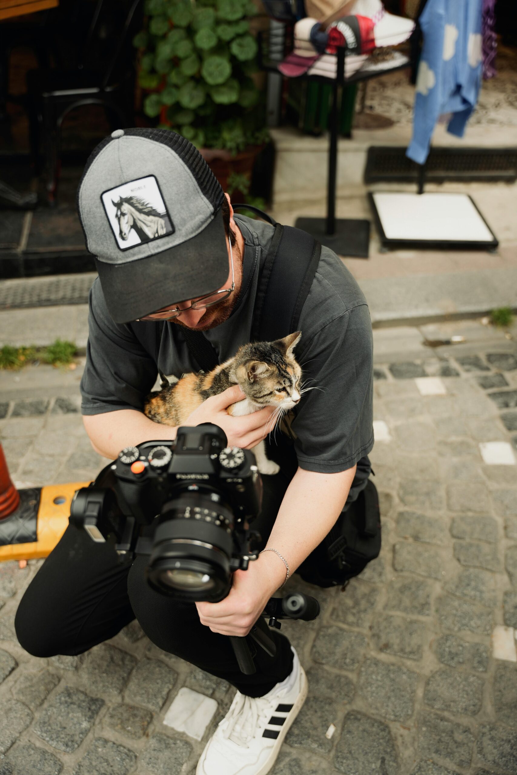 A photographer crouches with a kitten during a city street shoot, capturing a candid moment.